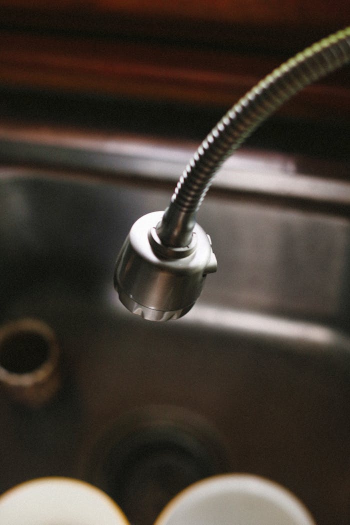 Detailed view of a flexible kitchen faucet illuminated over a stainless steel sink.